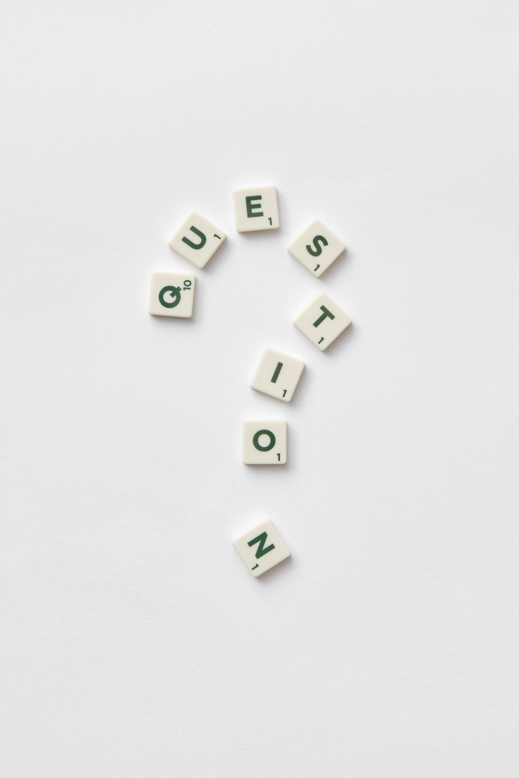 Artistic arrangement of letter tiles forming a question mark on a white background.