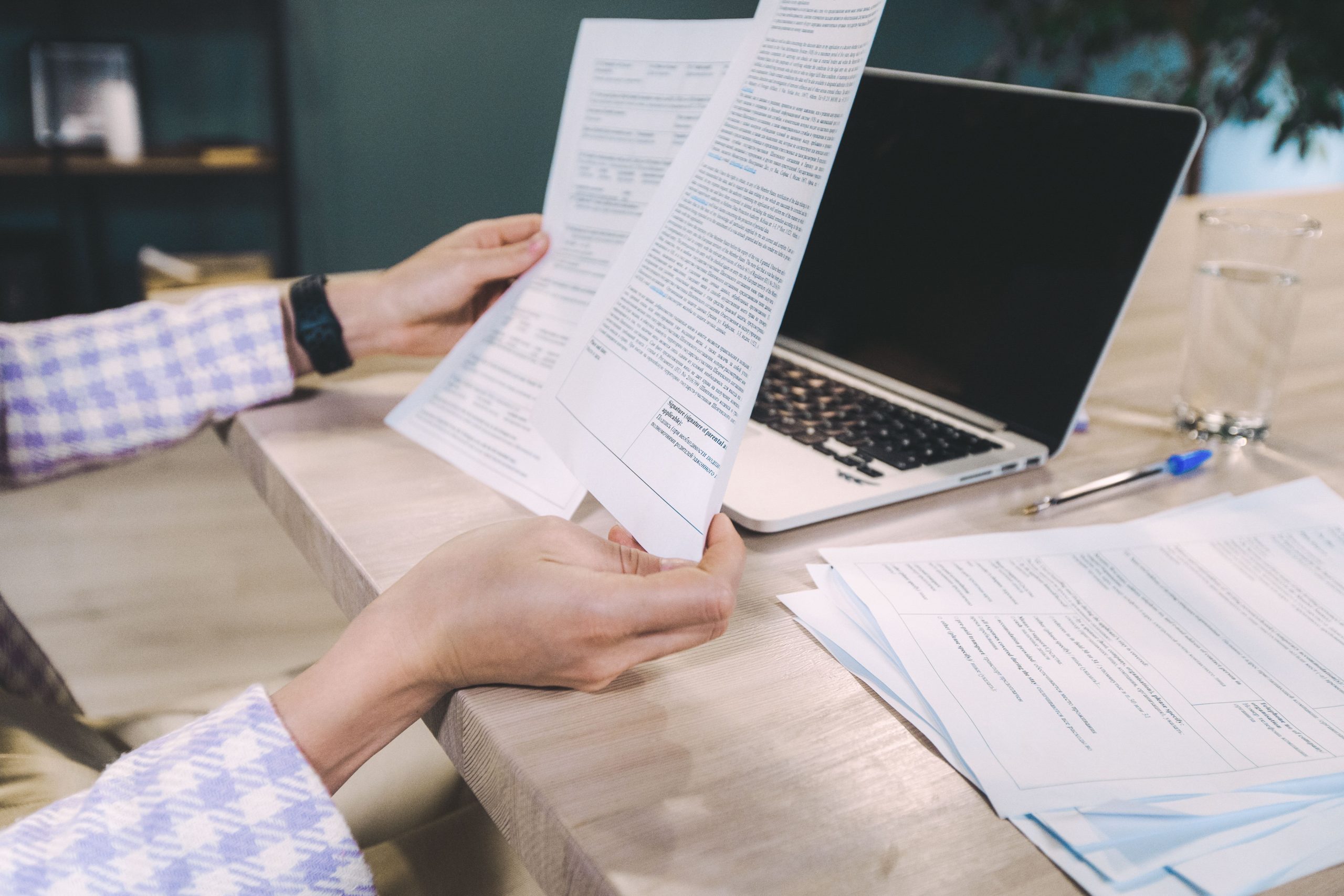 Close-up of hands examining printed documents next to laptop on office desk.